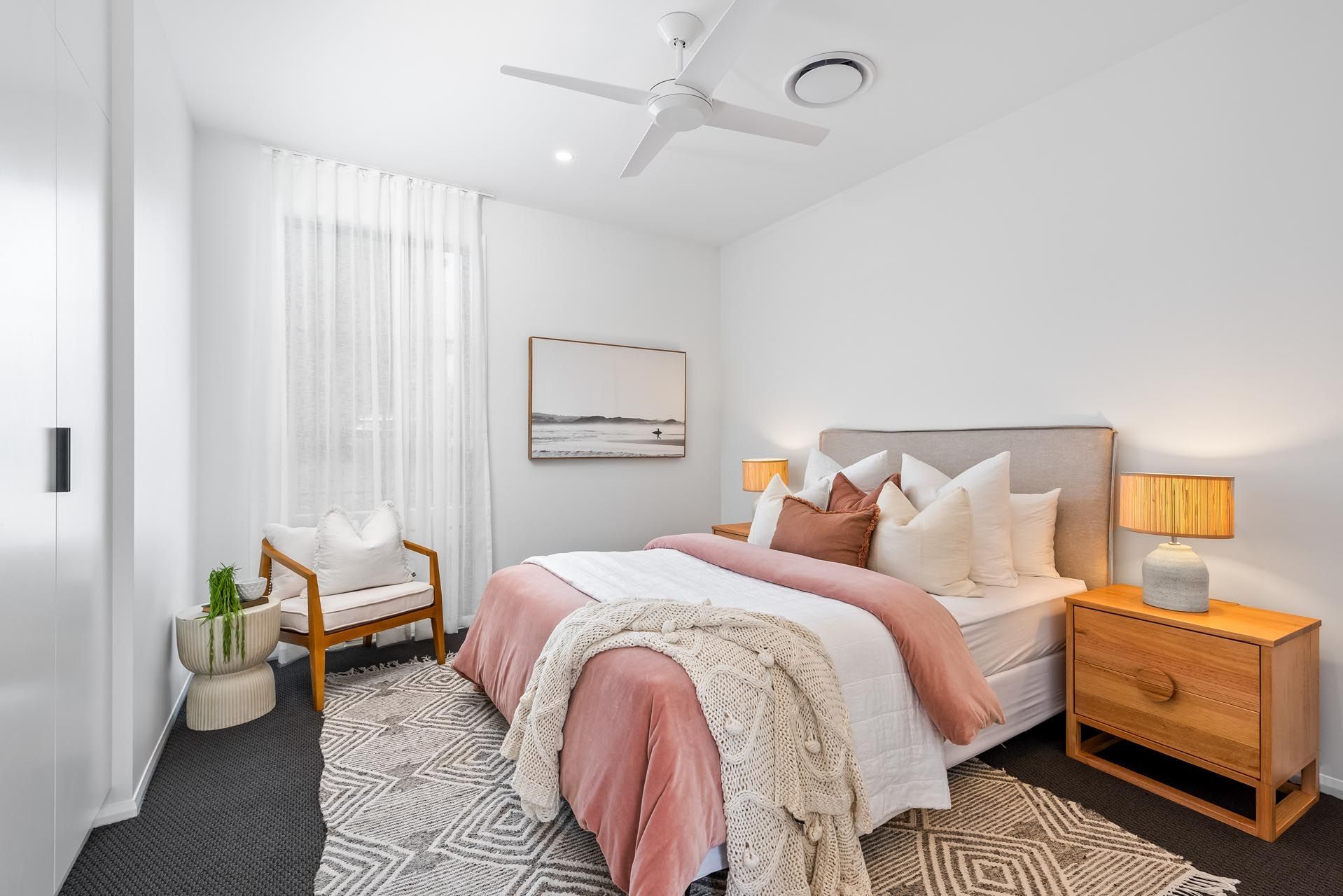 A bedroom with a bed , nightstand , chair and ceiling fan.