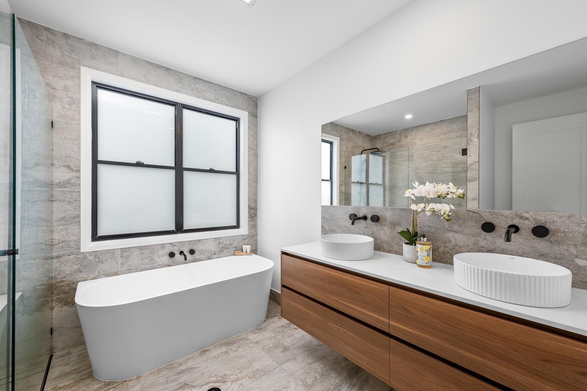 A bathroom with two sinks , a tub , and a window.
