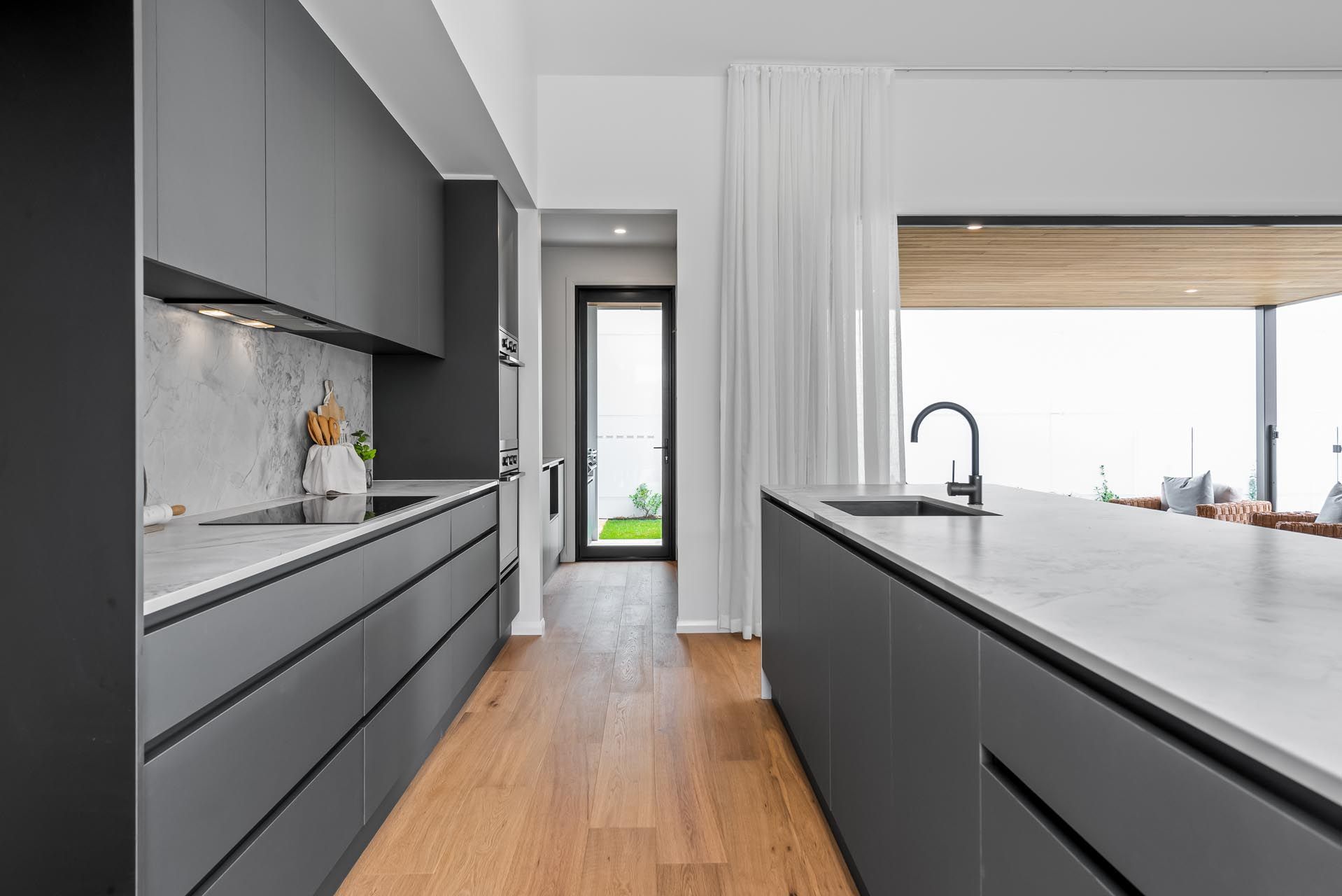 A kitchen with grey cabinets , white counter tops , and wooden floors.