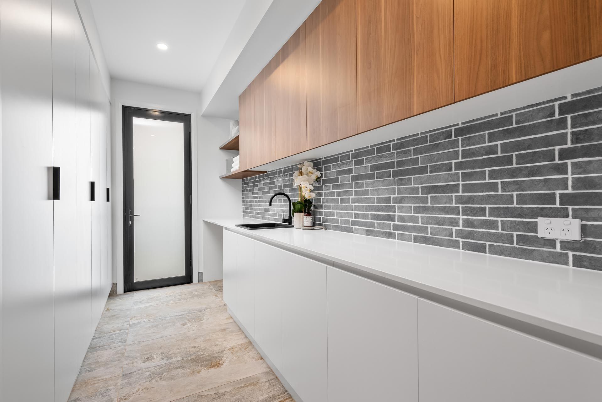 A kitchen with white cabinets and wooden cabinets and a brick wall.