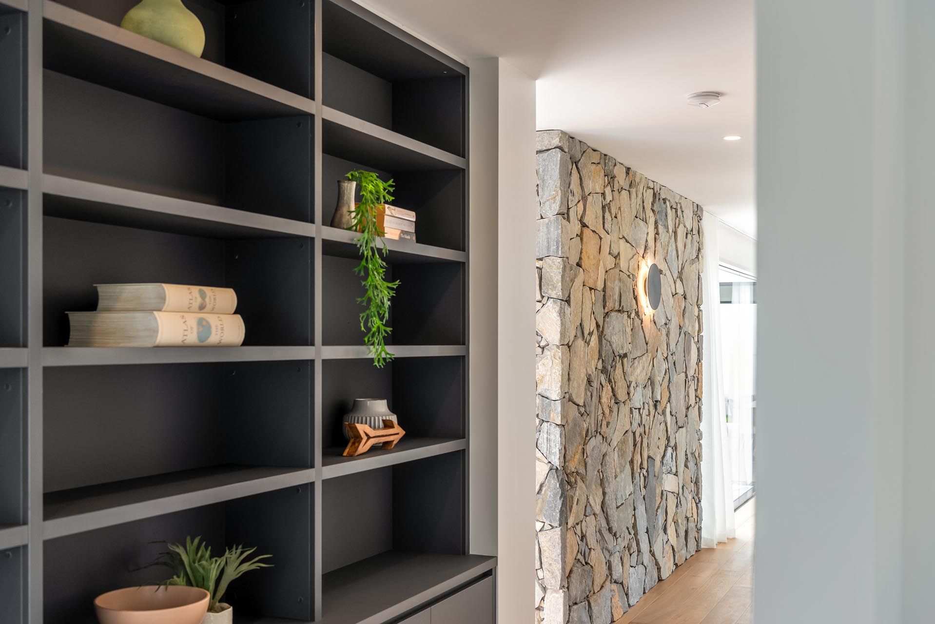 A hallway with a stone wall and shelves filled with books and vases.