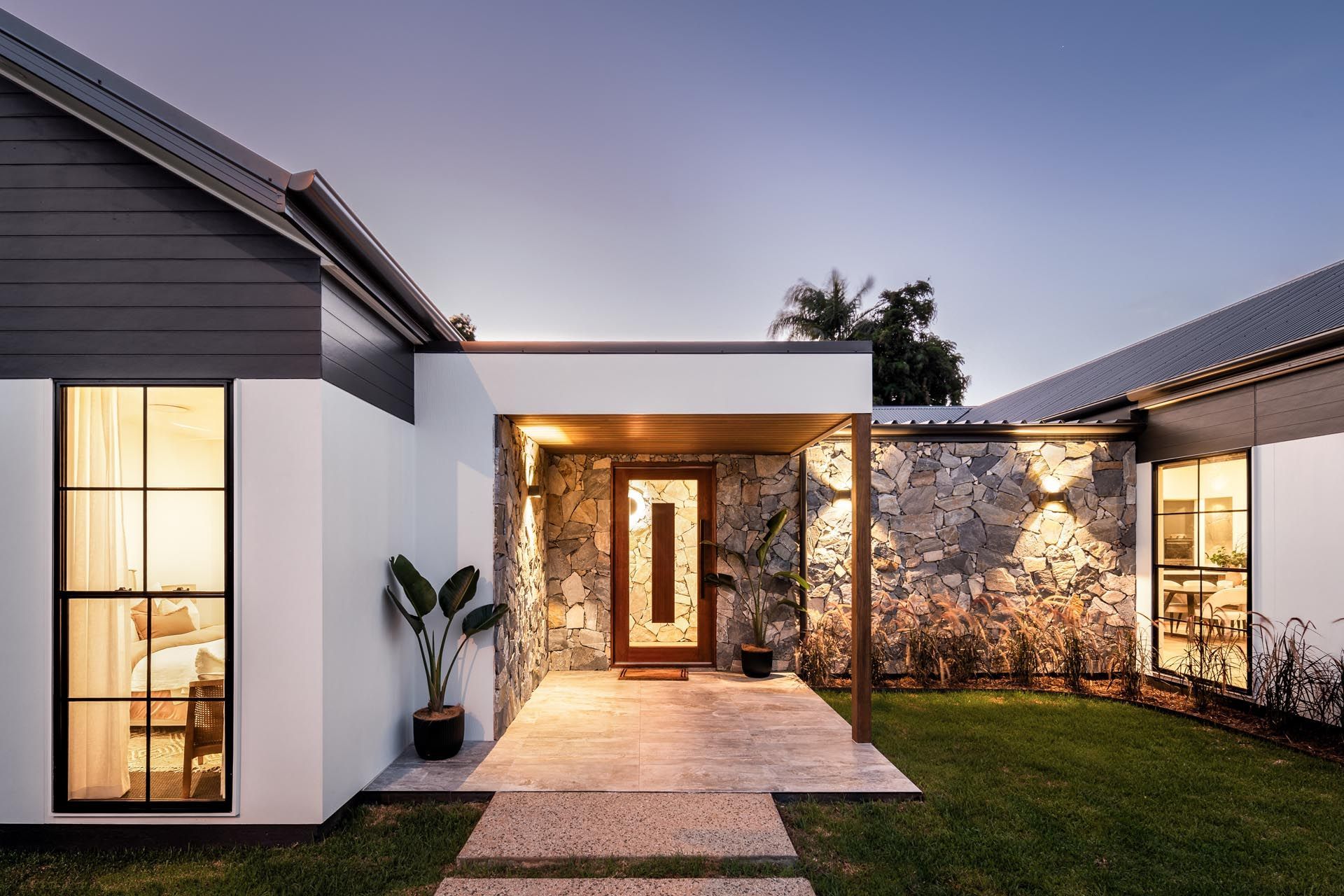 A modern house with a stone wall and a walkway leading to the front door.