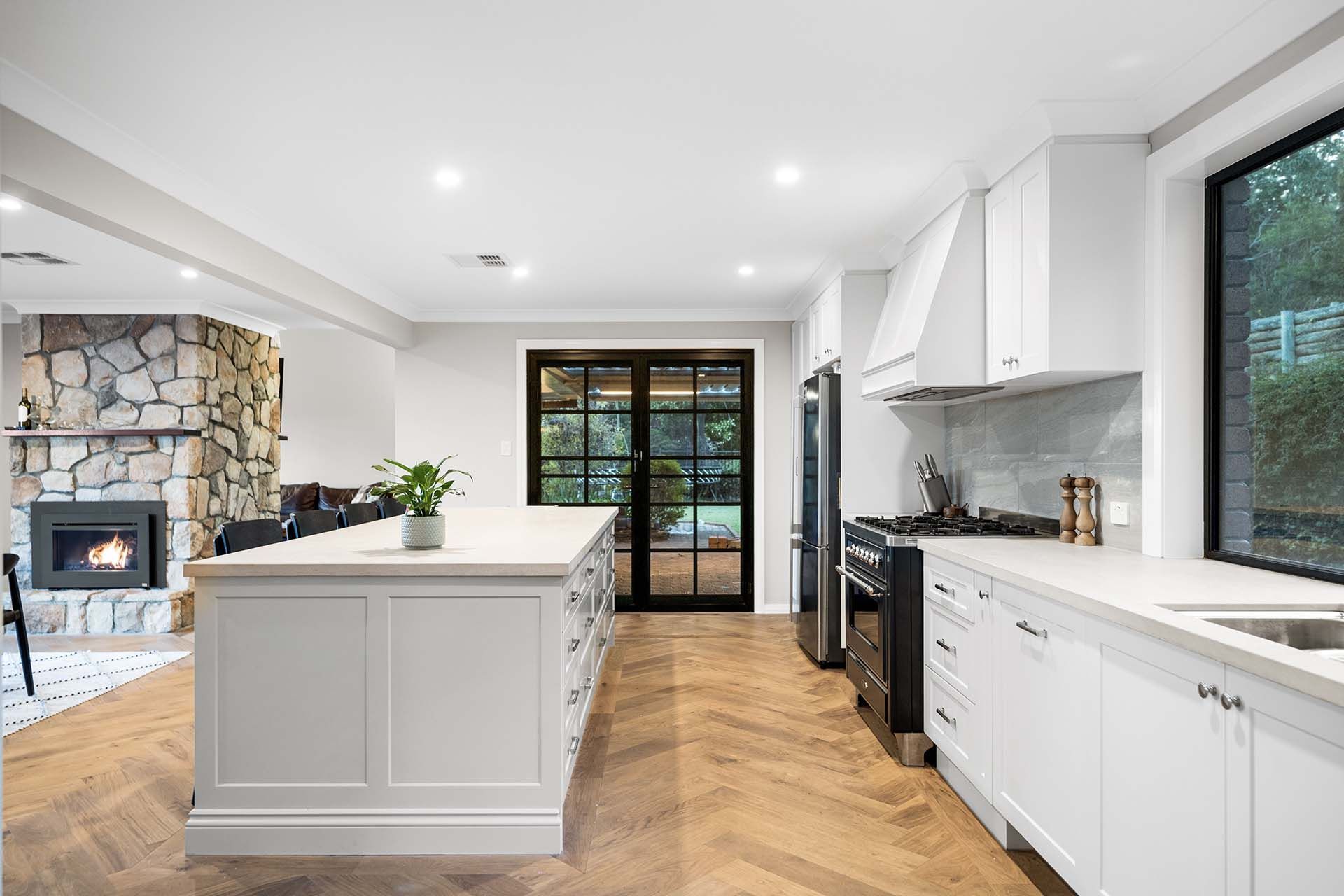 a kitchen with white cabinets , stainless steel appliances , a large island and a fireplace .