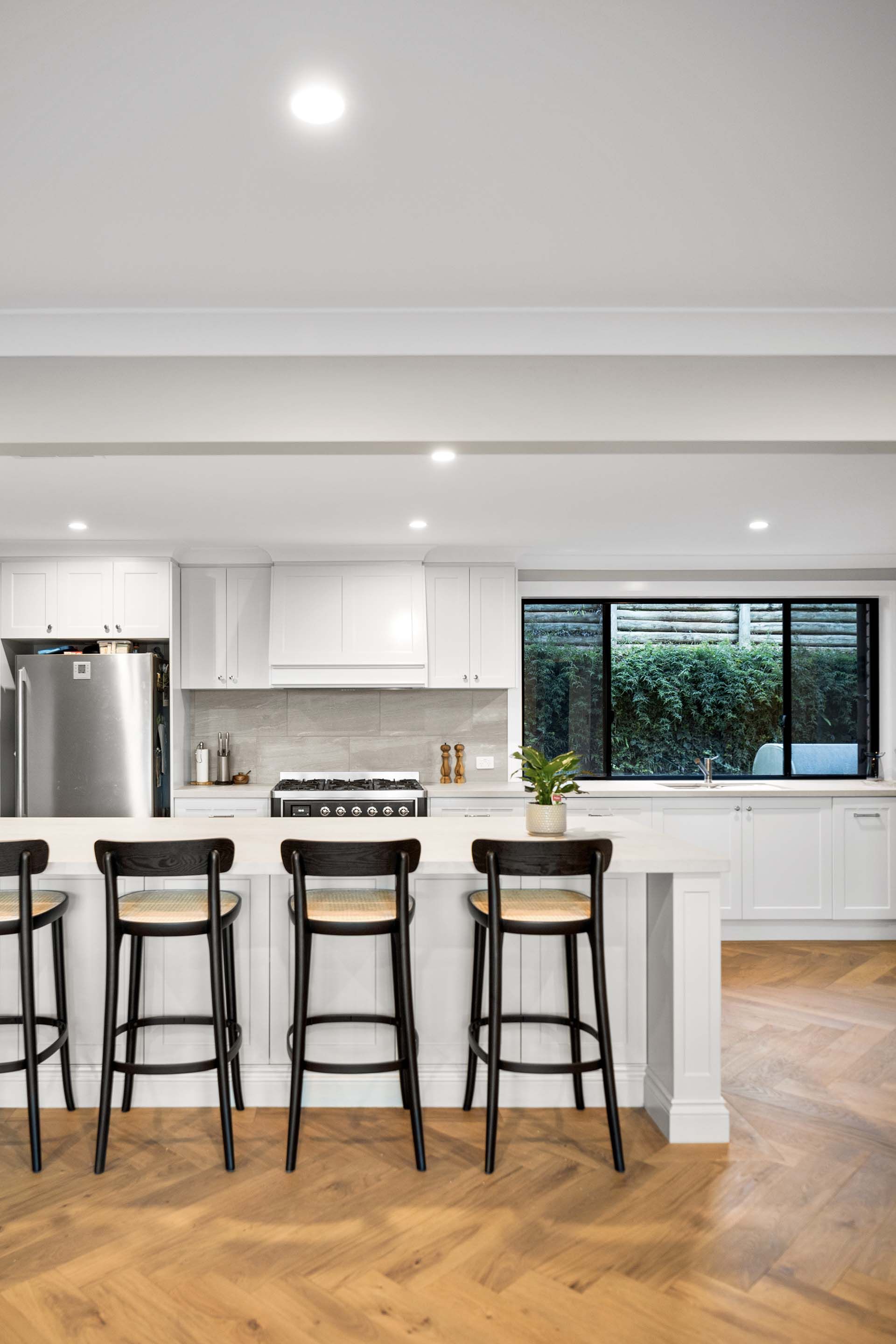 a kitchen with white cabinets , a stove , a refrigerator , a bar and stools .