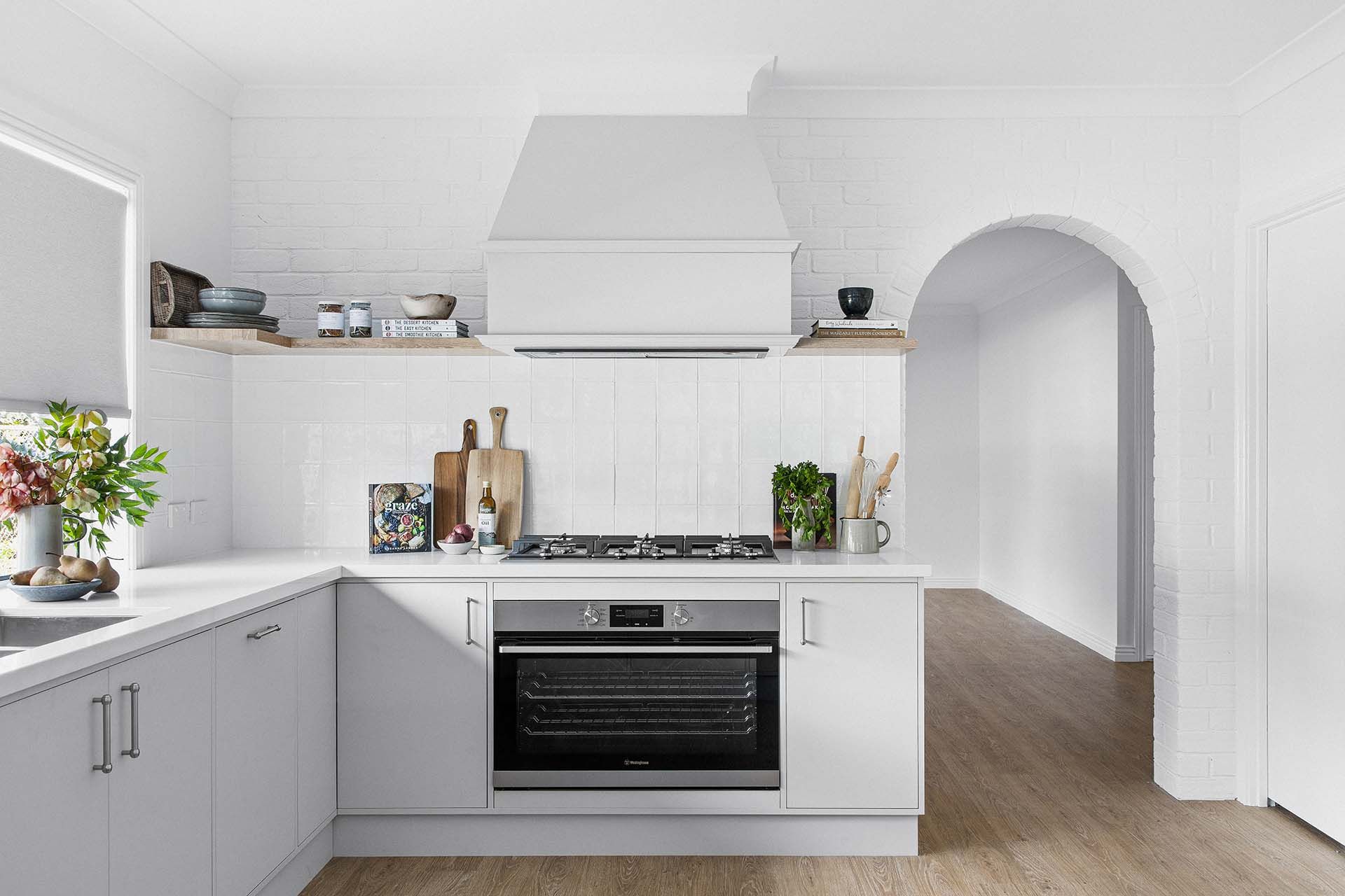 a kitchen with white cabinets , a stove top oven , a sink , and a hood 