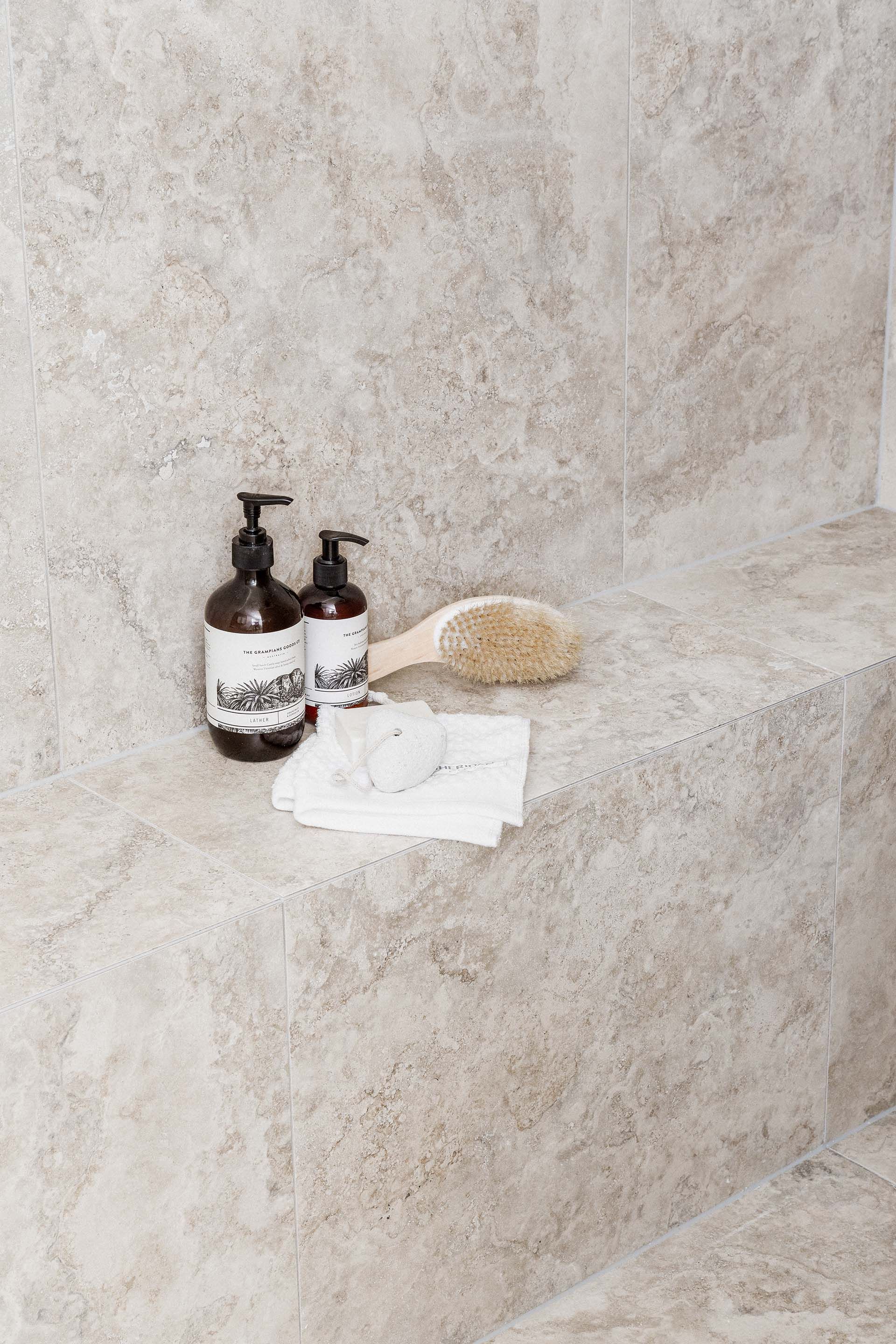 there are two bottles of soap and a brush on the ledge .