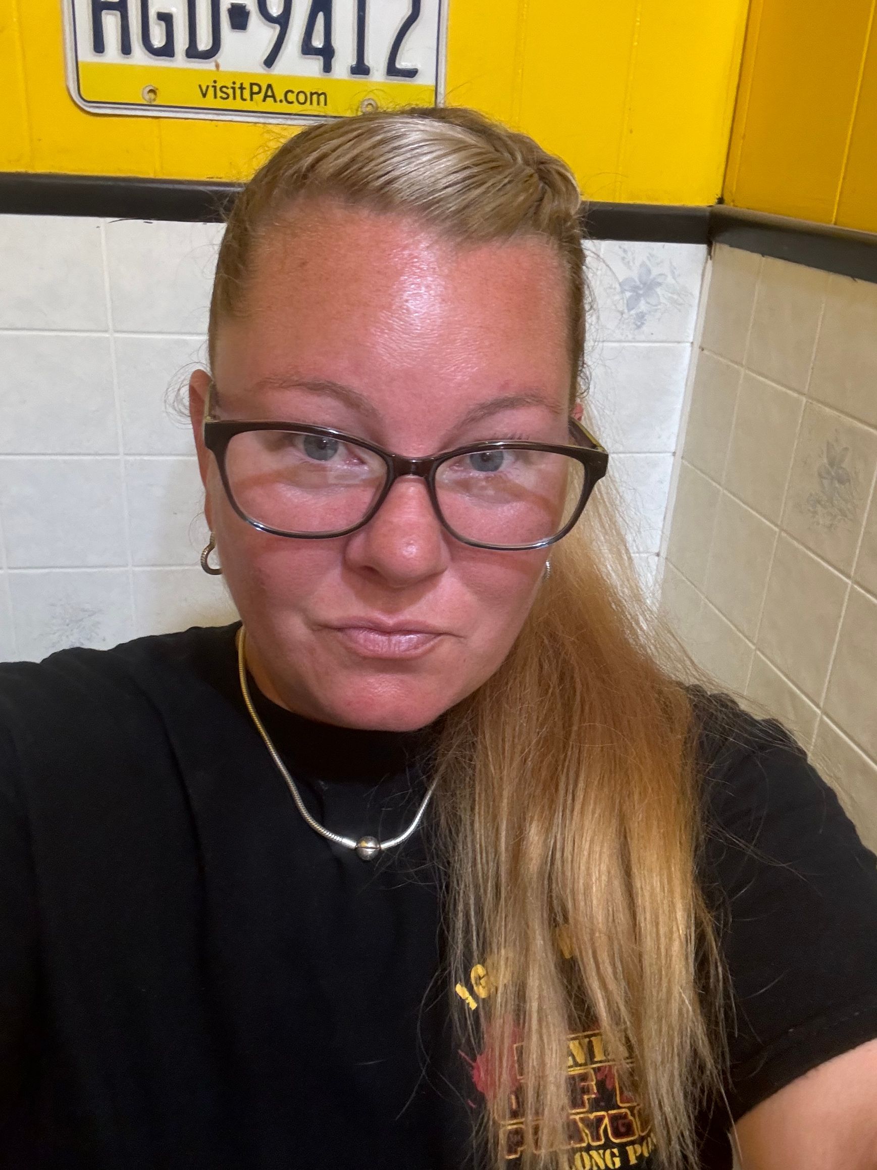 A woman wearing glasses and a black shirt is taking a selfie in a bathroom.