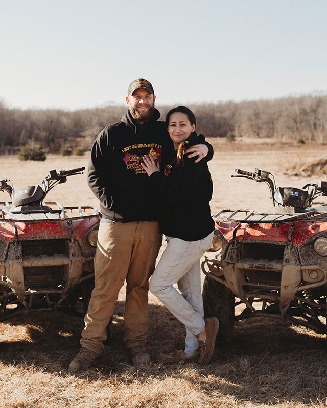 A man and a woman are standing next to atvs in a field.