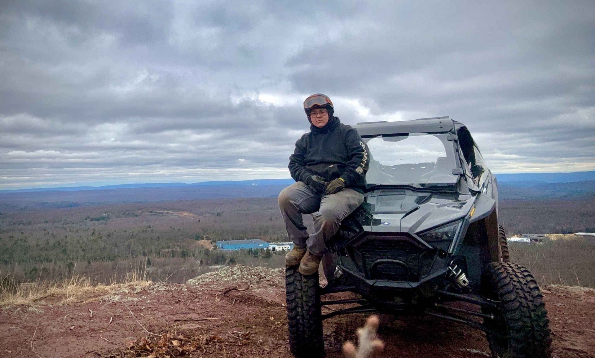 A man is sitting on the front of a atv on top of a hill.