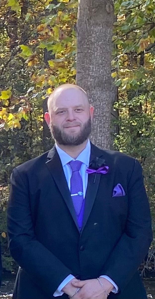A man in a suit and tie is standing in front of a tree.