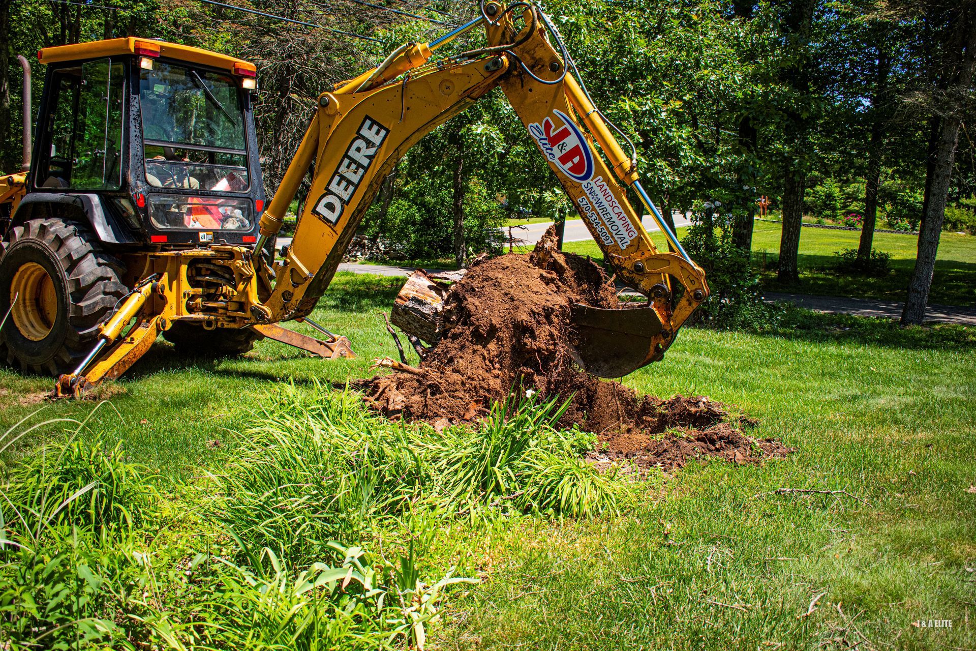 A yellow deere backhoe is digging a hole in the grass.
