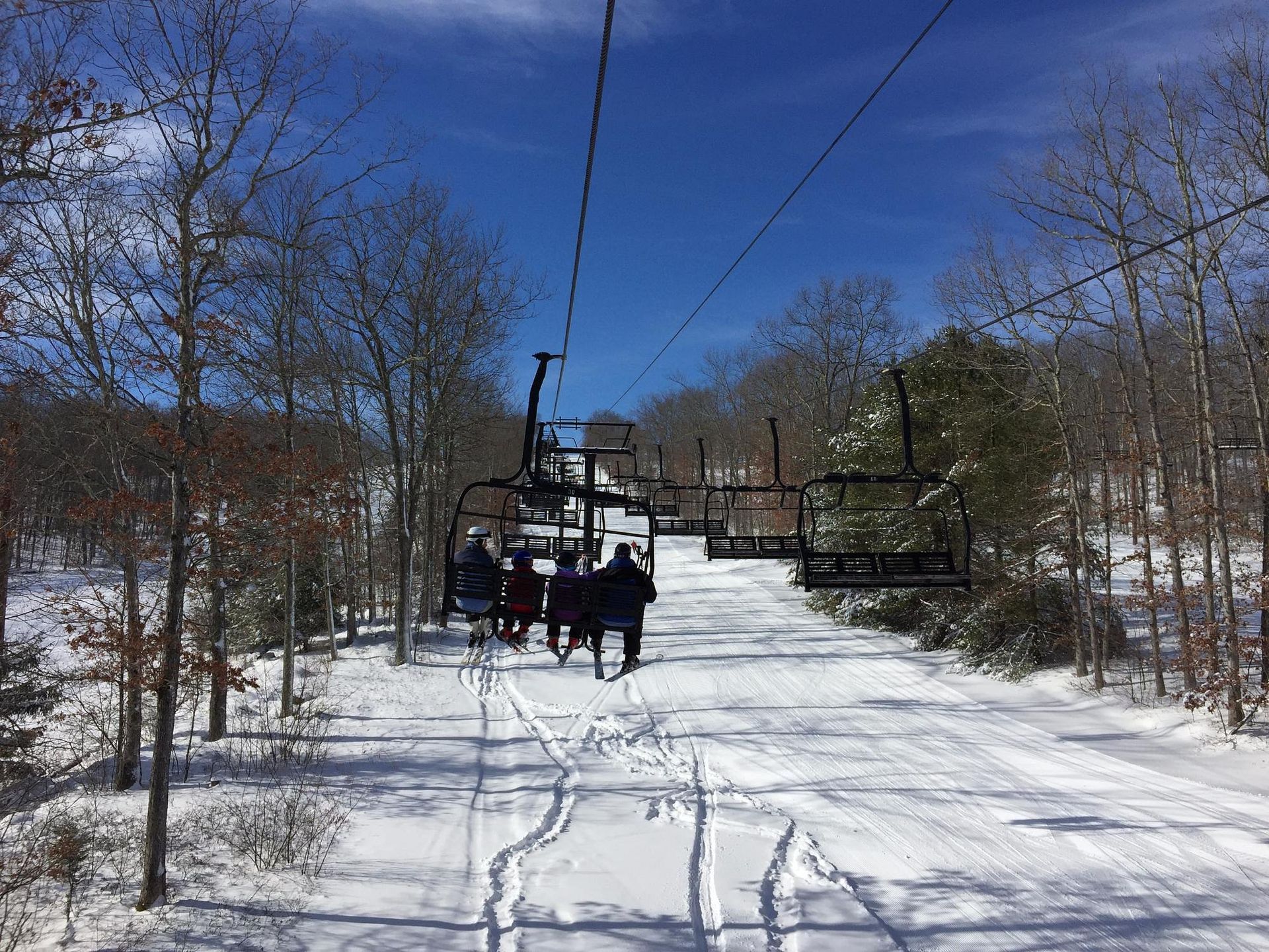 A group of people are riding a ski lift down a snow covered slope.