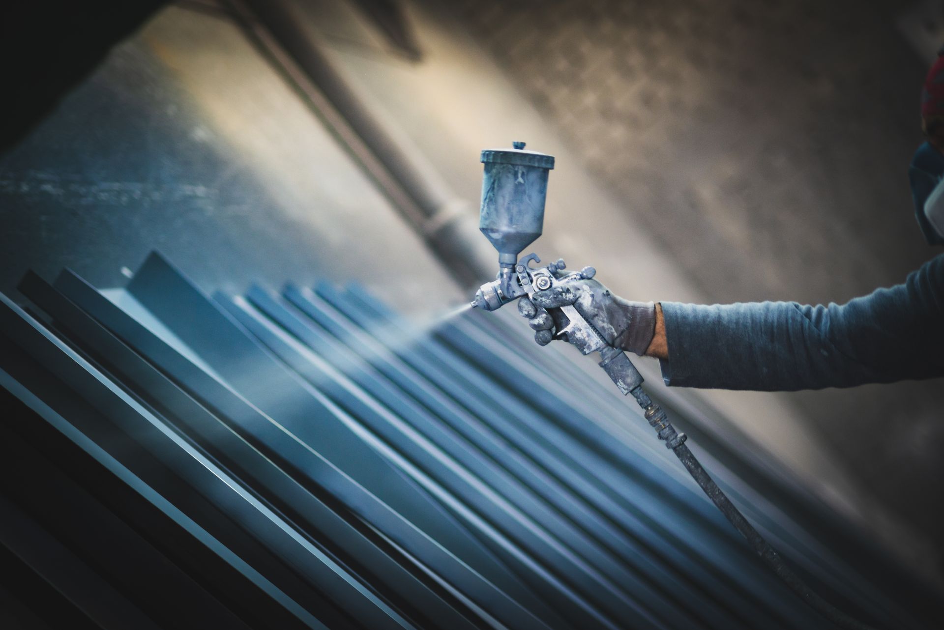 A man wearing protective gear is applying industrial paint to metal products using a spray gun.