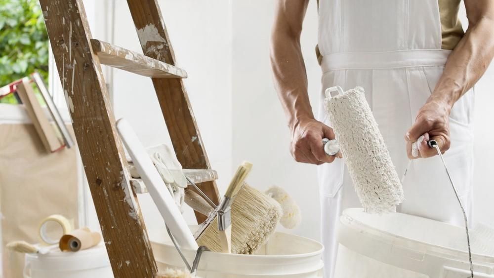 A man is holding a paint roller in front of a ladder.