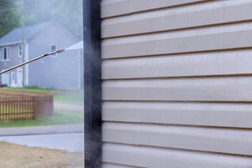 A person is cleaning the side of a house with a pressure washer.