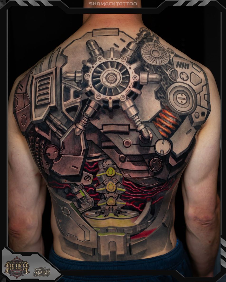 Side view of a tattooed arm with a blue shield tattoo, wearing a black sleeveless shirt and jeans.