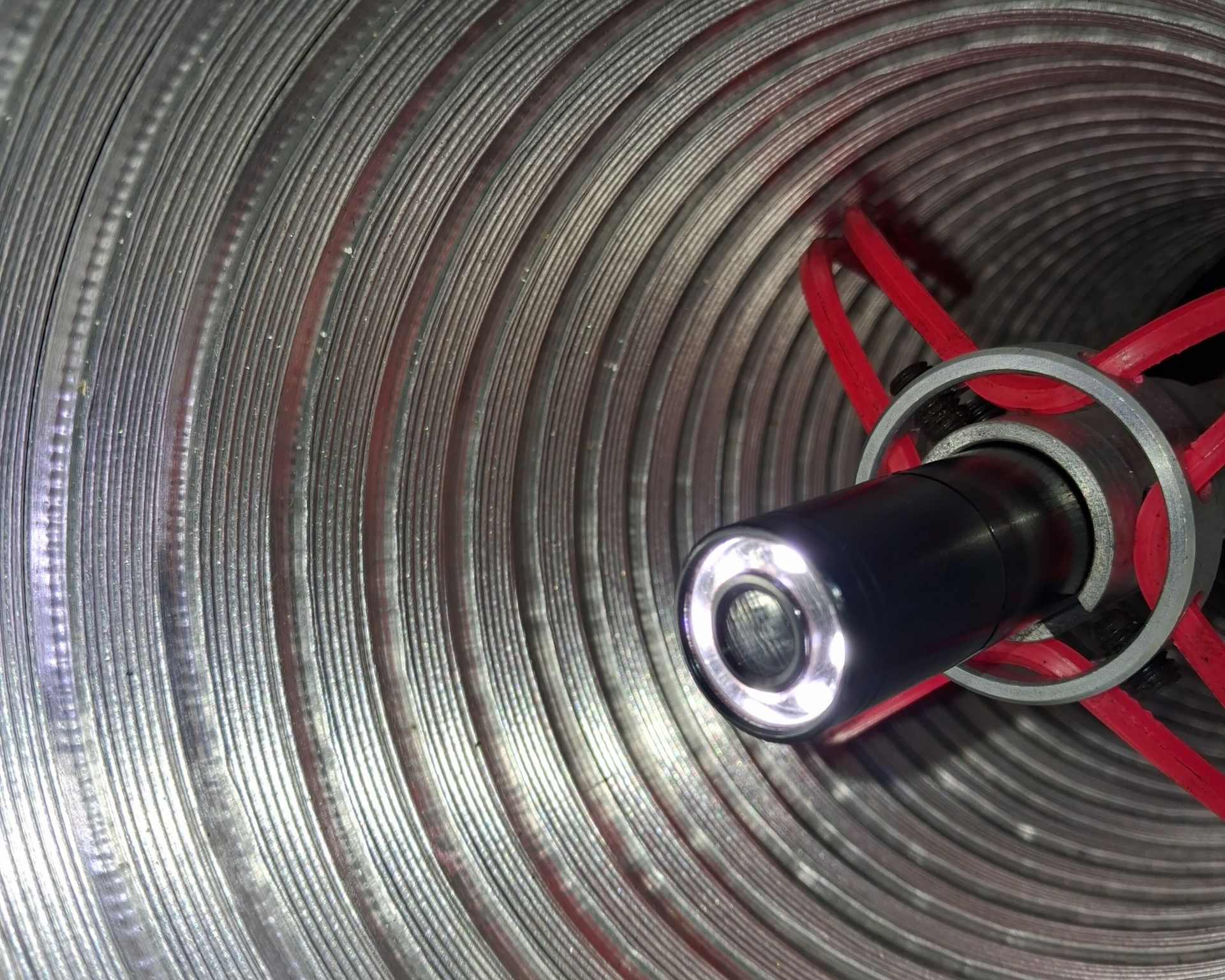 Une caméra avec une lumière à l'intérieur d'un tube métallique ondulé, probablement pour l'inspection.