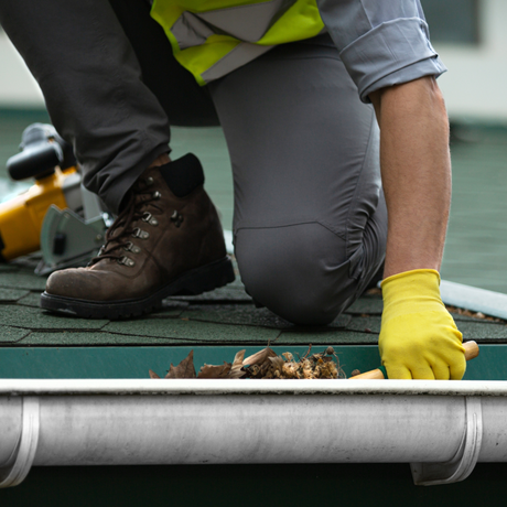 Paradise Home Services | a man wearing yellow gloves is cleaning a gutter on a roof