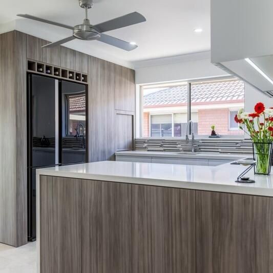 A Kitchen With Wooden Cabinets, a Ceiling Fan, a Sink, and a Refrigerator — PKJ Designs in Unanderra, NSW