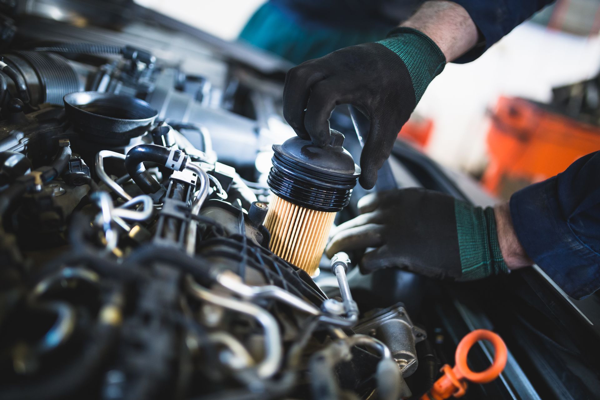 A mechanic in black gloves installs a cylindrical car engine oil filter.