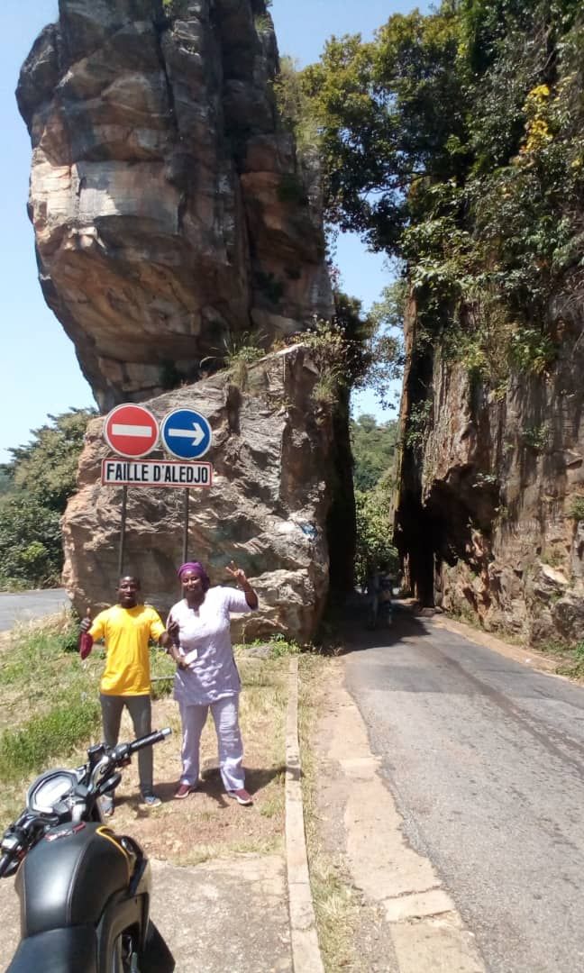 Two men are standing next to a motorcycle on the side of a road.