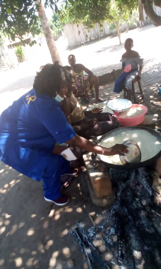 A woman in a blue shirt is cooking food on a stove outside.