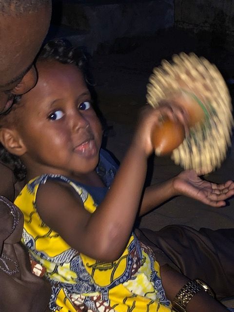 A little girl in a yellow dress is playing a drum