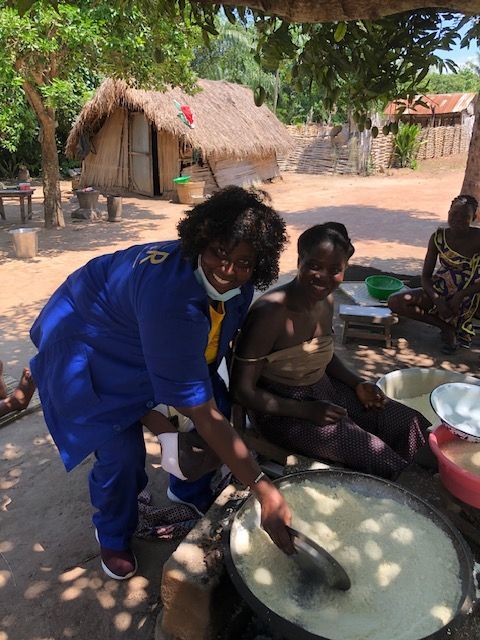 A woman wearing a mask is standing next to a woman making food.