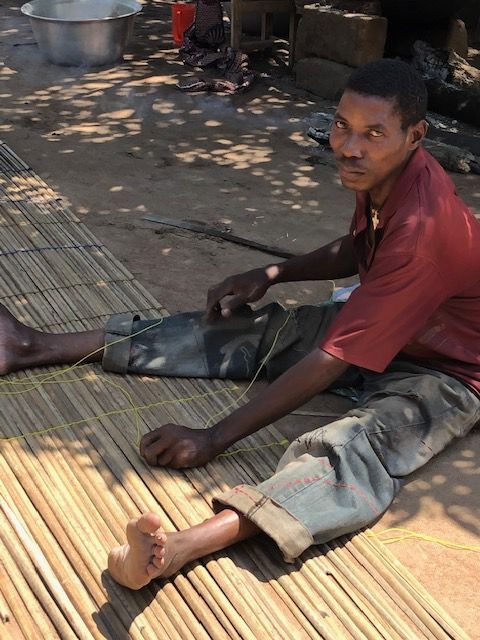 A man in a red shirt sits on a bamboo mat