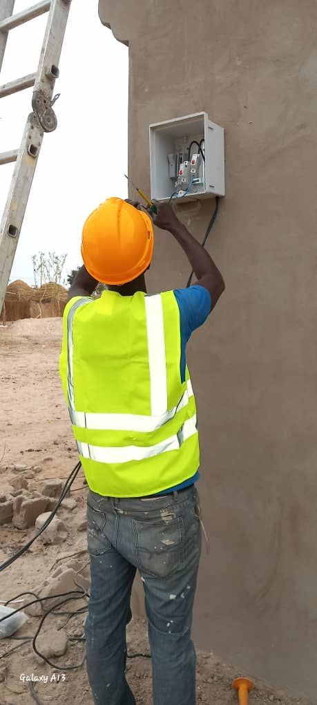 A man wearing a hard hat and safety vest is working on a box on a wall.
