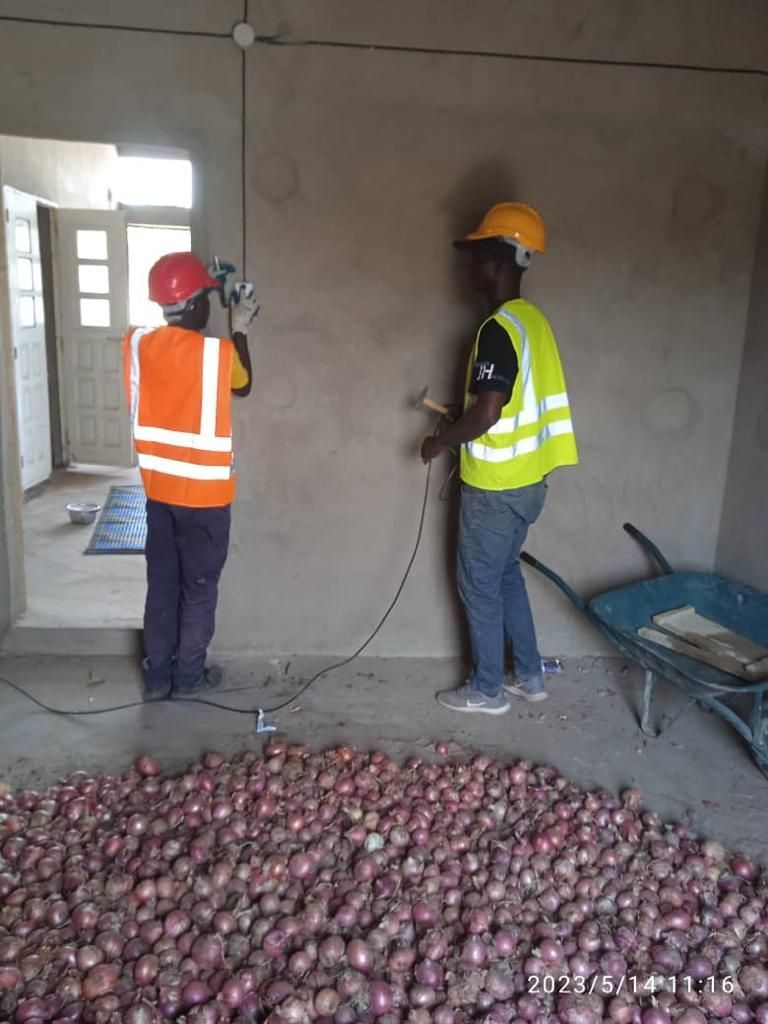 Two construction workers are working on a wall next to a pile of onions.