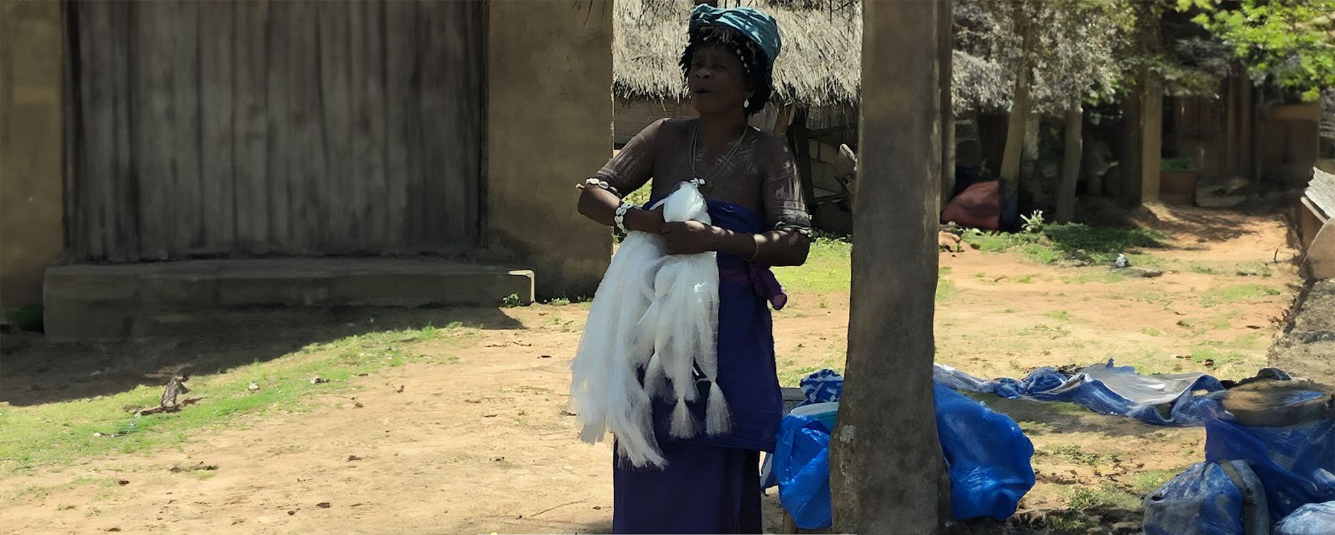 A woman in a purple dress is standing next to a tree holding a bunch of feathers.