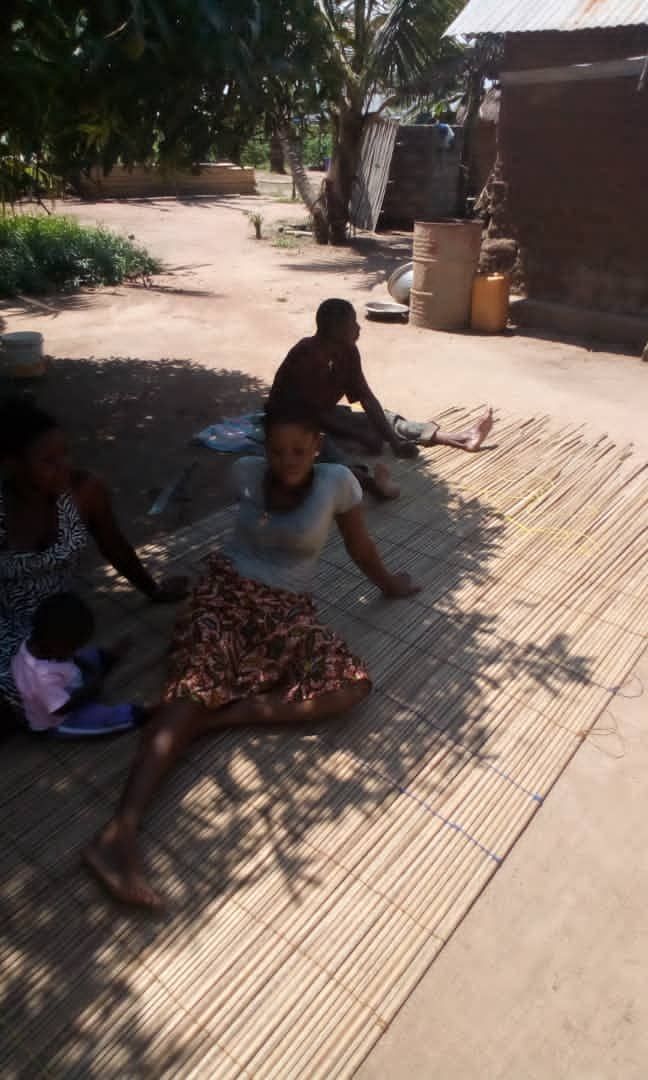 A group of people are sitting on a mat on the ground.