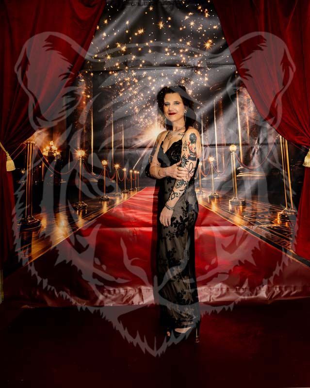 A person in a black gown stands before a red carpet backdrop with gold lights and a faint tiger watermark overlay.