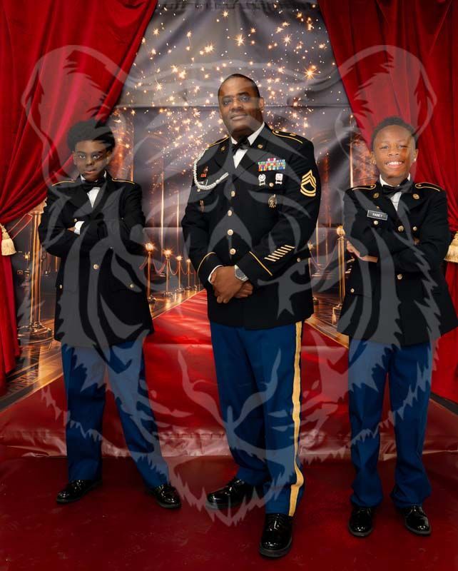 A person in a military uniform stands between two people in formal military-style dress against a red curtain background.