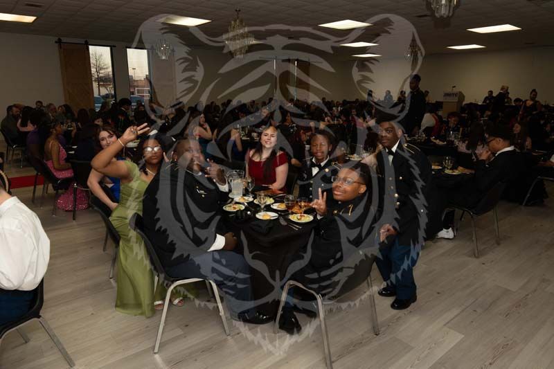A group sits at a decorated table in a large banquet hall, smiling and posing for a photo during a formal event.