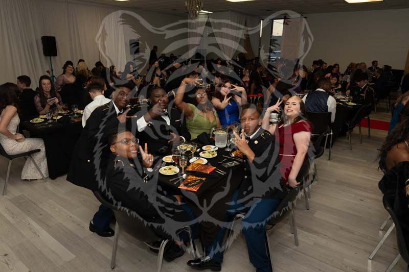 A group of people sitting at a table at an event, some posing for a photo while eating at a banquet in a dining hall.