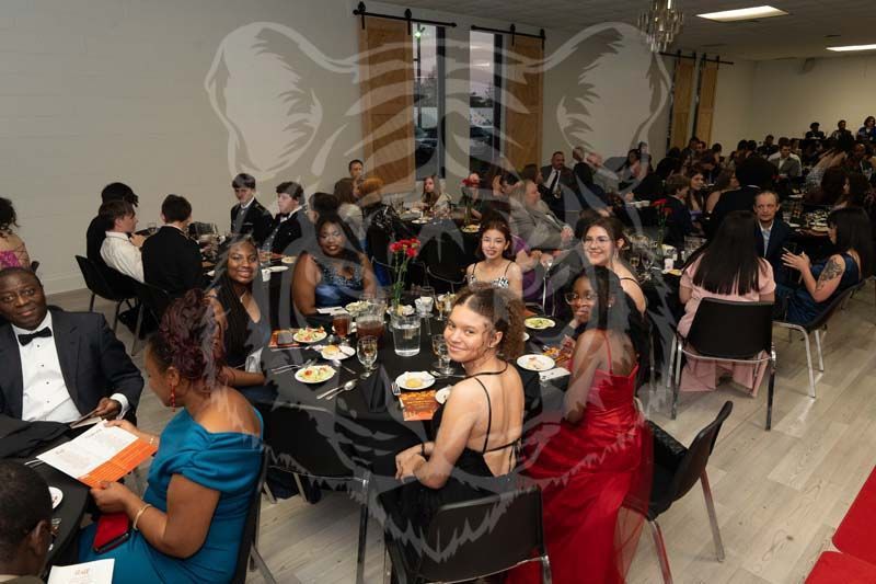 Guests at a banquet hall wearing formal attire, seated at round tables for a dinner event.