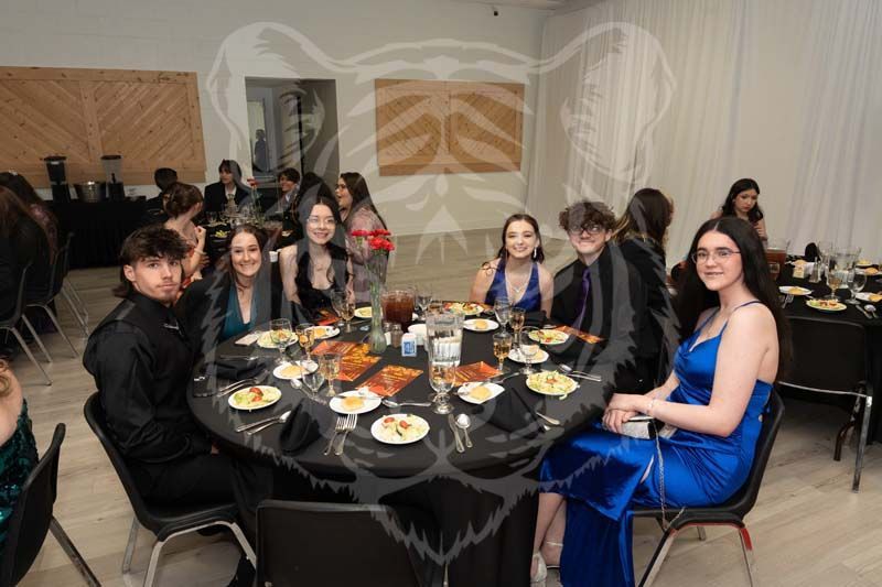 A group of people sitting at a round table with black linens and place settings during a formal event in a hall.