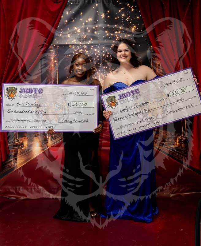 Two individuals in formal gowns hold large JROTC scholarship checks on a red carpet in front of a curtain backdrop.