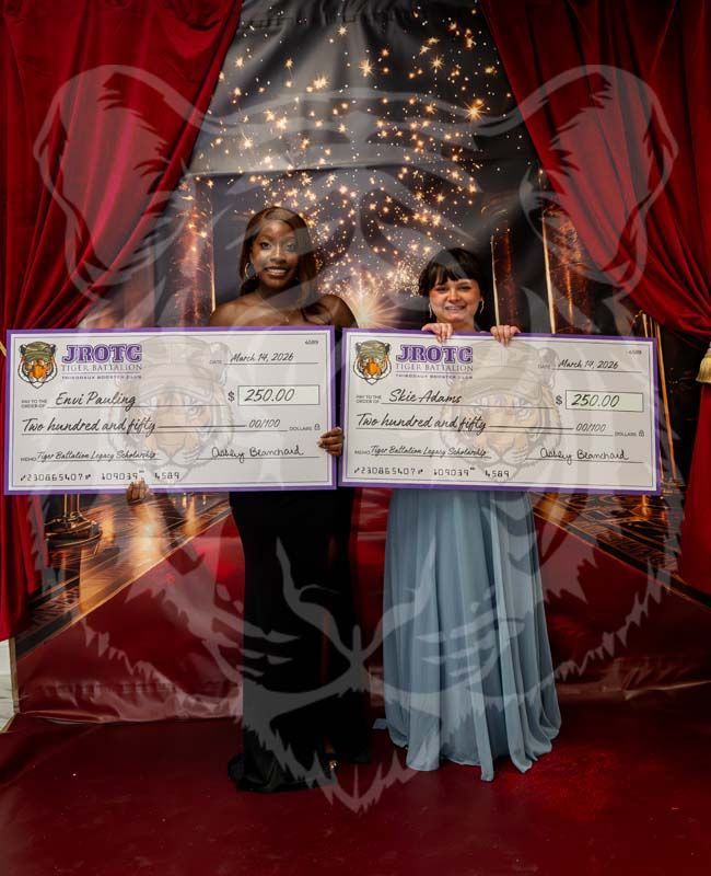 Two people in formal attire hold large JROTC scholarship checks in front of a stage-style curtain backdrop.