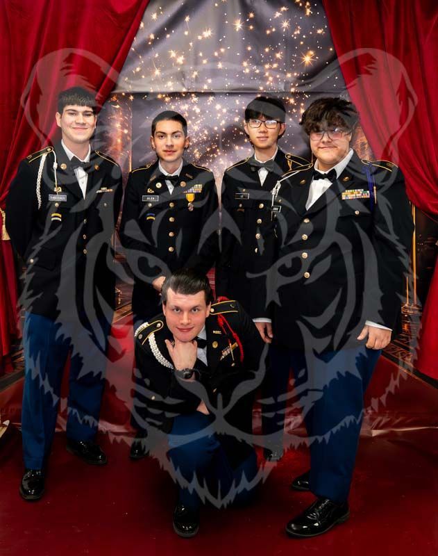 Five individuals in formal military dress uniforms pose in front of a red curtain, with one kneeling in the center.