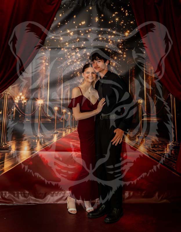 A couple poses on a red carpet backdrop with festive lighting, overlaid with a faint, white tiger face graphic.