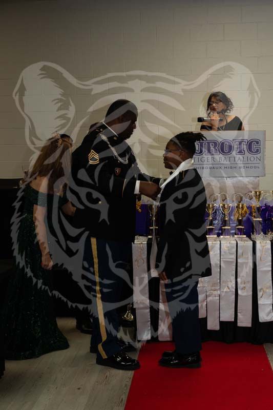 A formal ceremony where an individual in military uniform adjusts a neck accessory on a person wearing a matching suit.