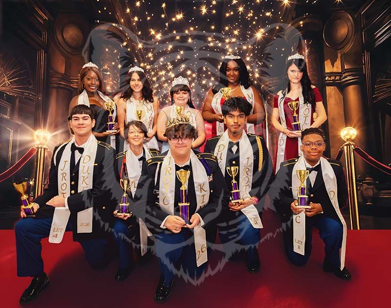 A group of individuals in formal attire and sashes pose with trophies on a stage with red carpet and a formal backdrop.