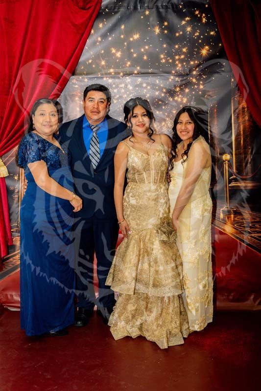 Four people pose in front of a red curtain and a starry backdrop. Everyone is smiling, dressed in formal attire.