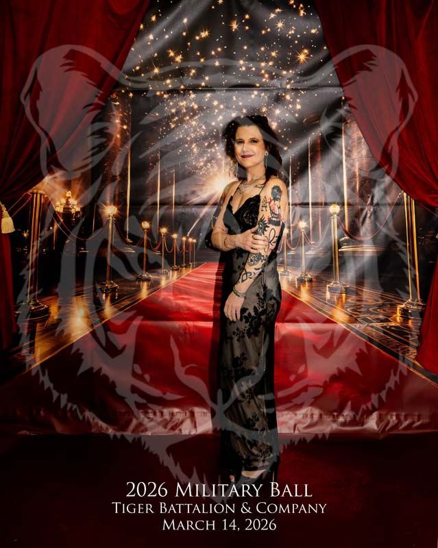 A woman in a black gown stands on a red carpet in front of a backdrop featuring a ghostly tiger and text for a 2026 ball.