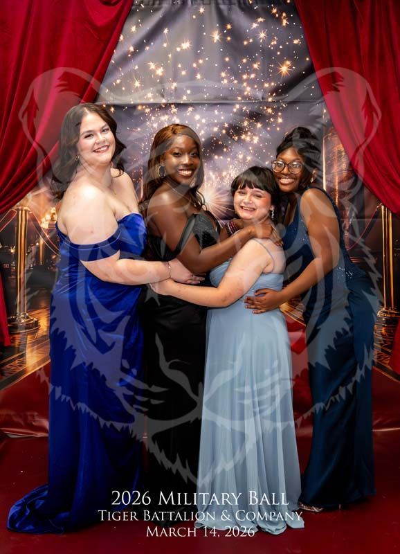 Four people in formal gowns pose together smiling in front of a red-curtained stage at the 2026 Military Ball.
