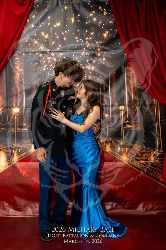 A couple in formal attire, a military uniform and blue dress, poses lovingly against a stage-like backdrop with red drapes.