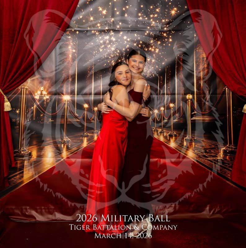 Two people in formal gowns hug on a red carpet in front of a red-curtained, festive stage at a 2026 military ball.